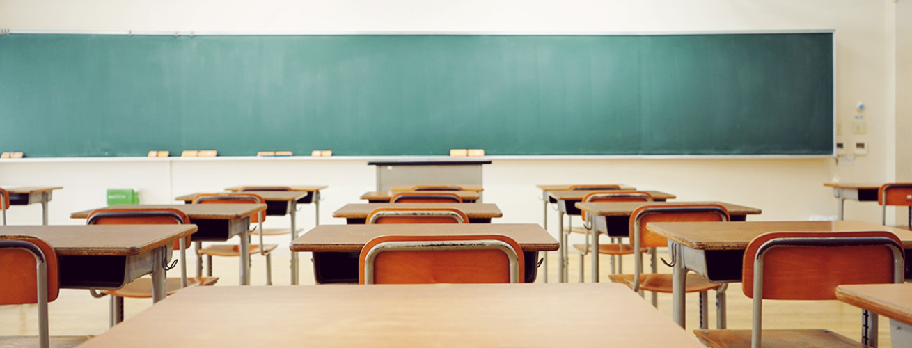 Classroom of empty desks facing a green chalkboard.
